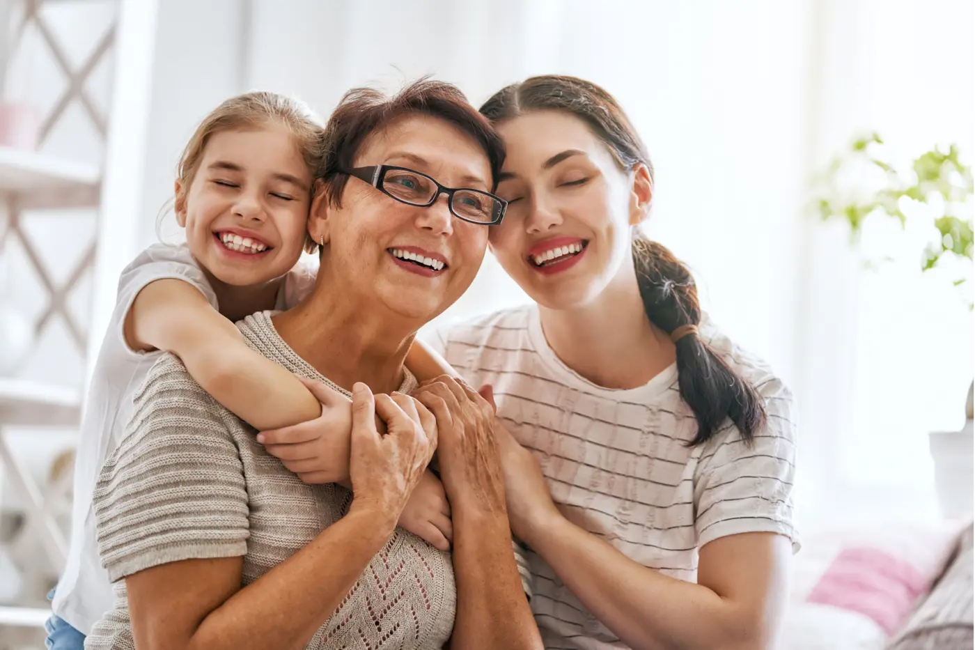 A grandmother, mother and daughter hugging and smiling together — dental care for every generation